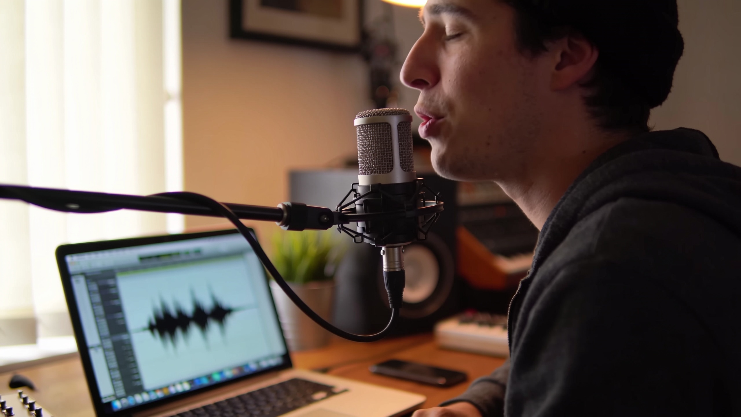 Person recording a jingle into a condenser mic with laptop waveform