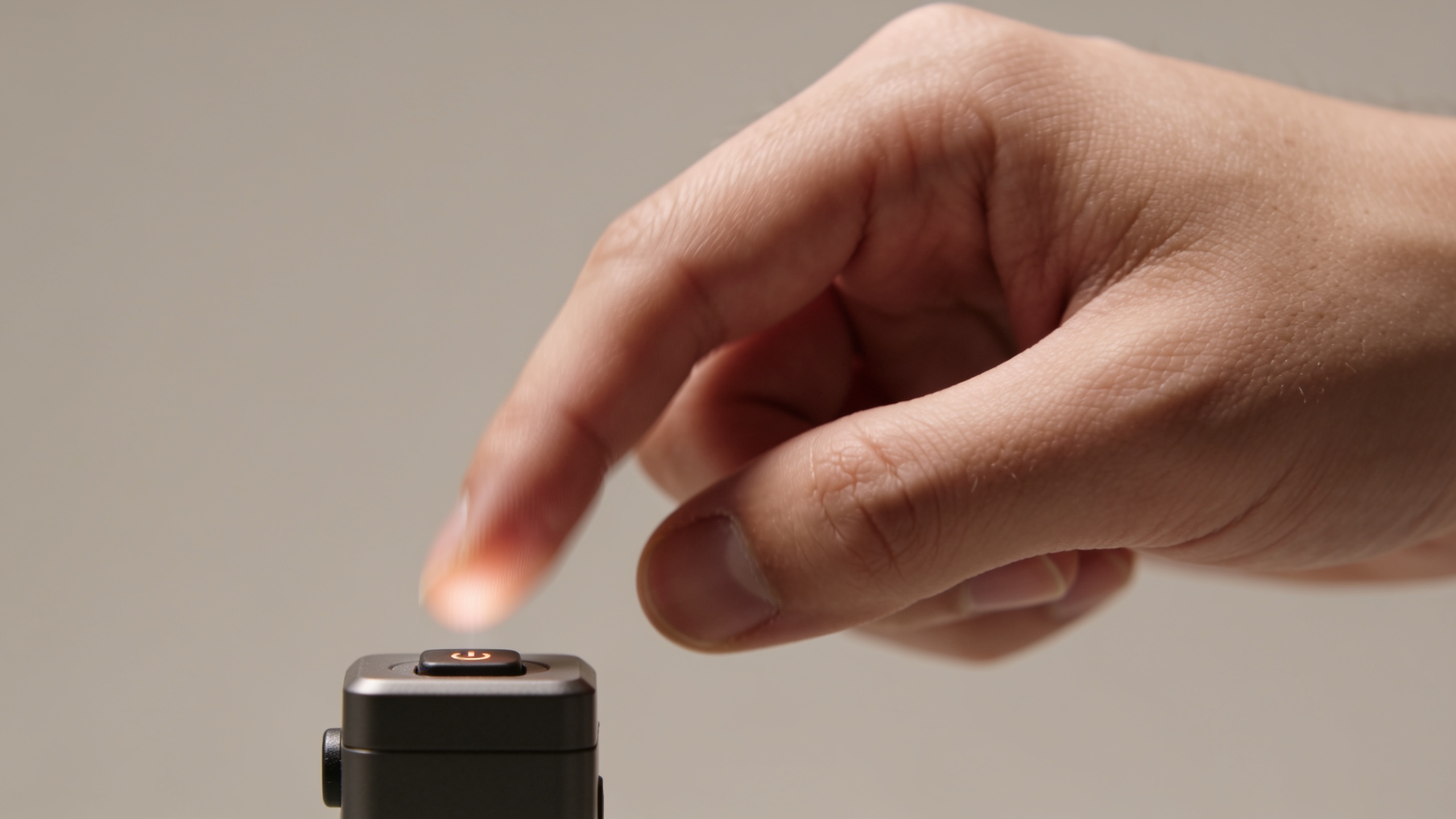 Hand pressing a button on a small device against a neutral background