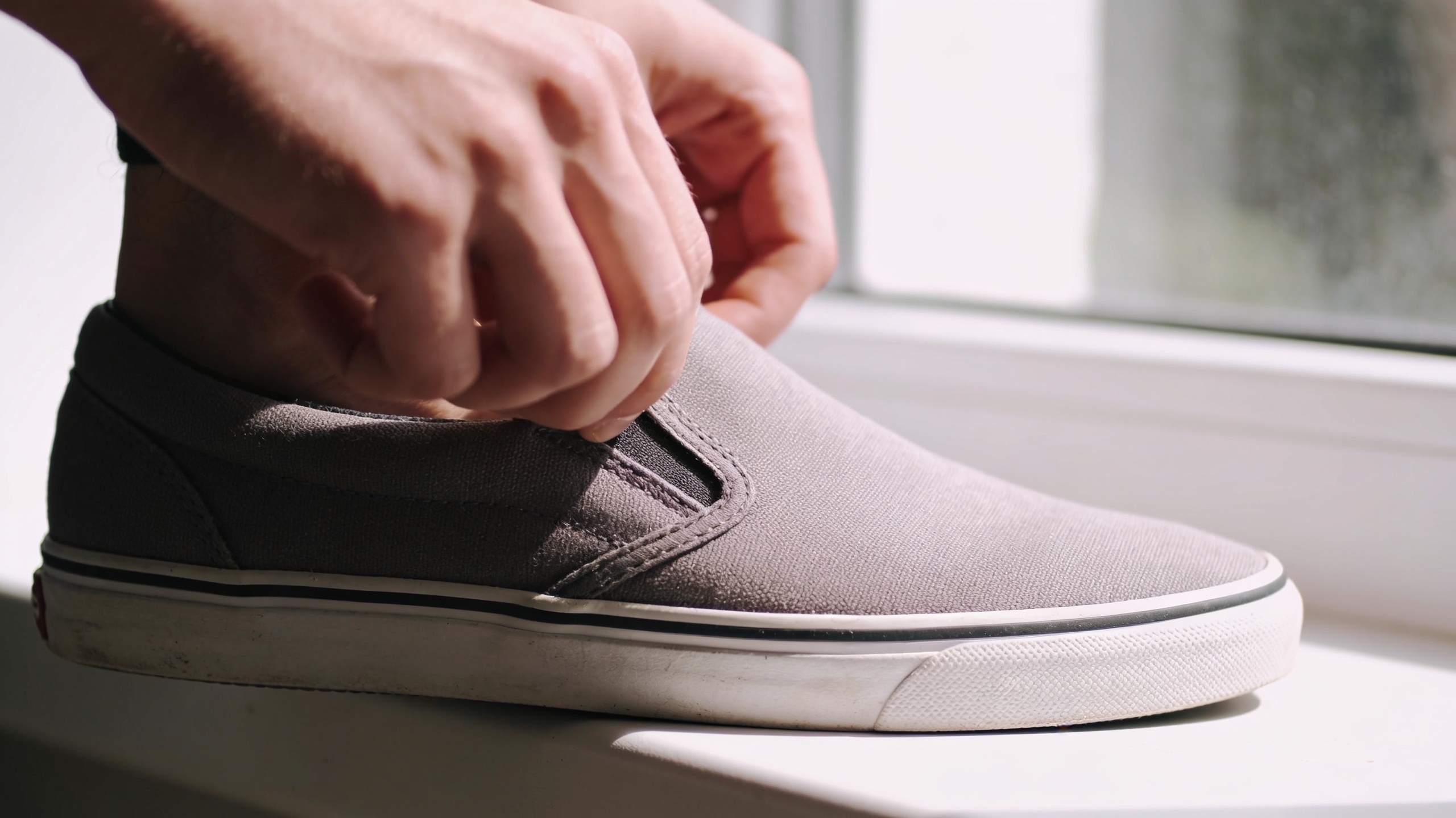 Hands pulling on a slip-on shoe in a vertical phone crop