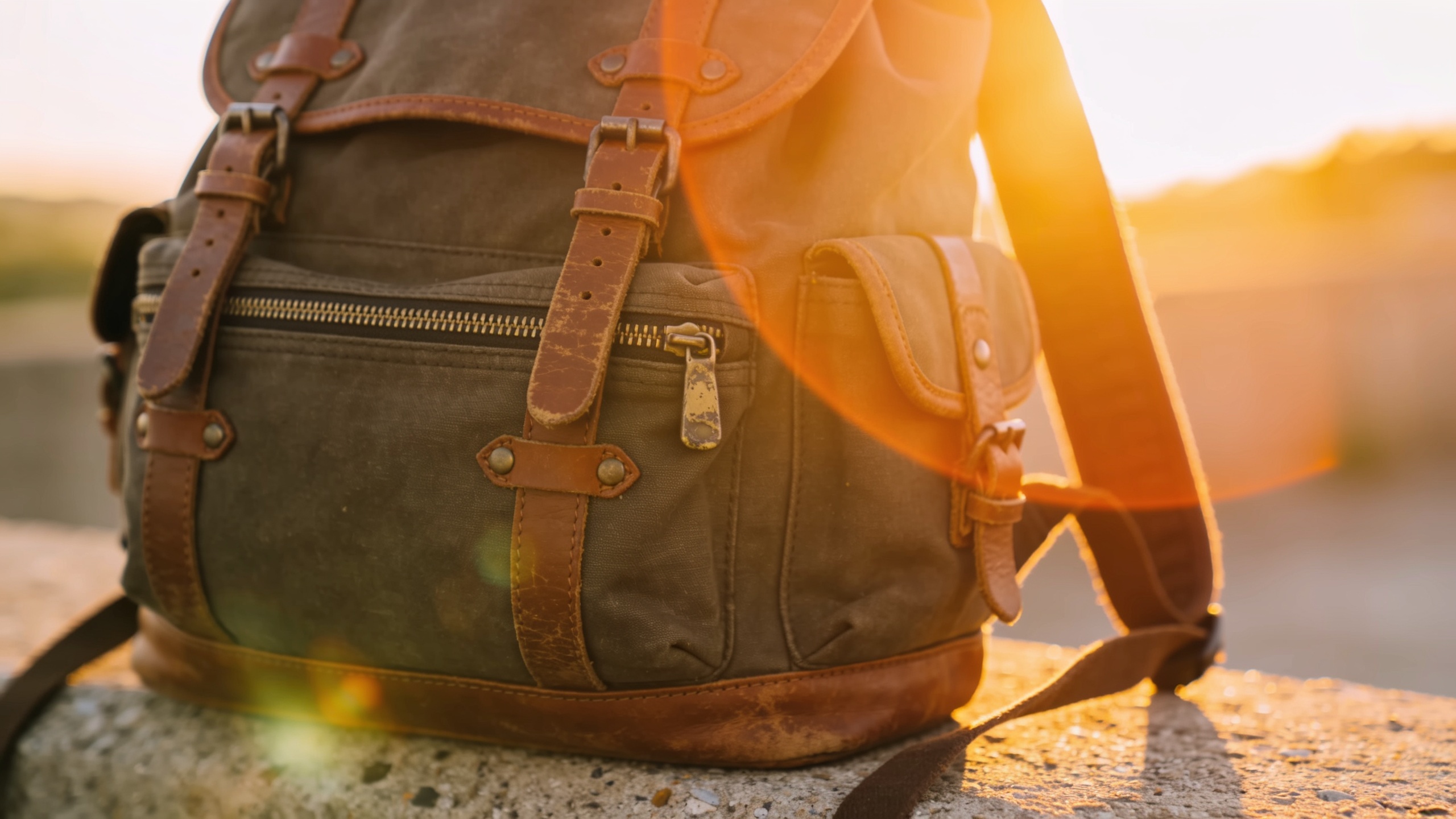 Lifestyle close-up of a travel backpack with golden-hour rim light on a textured concrete surface