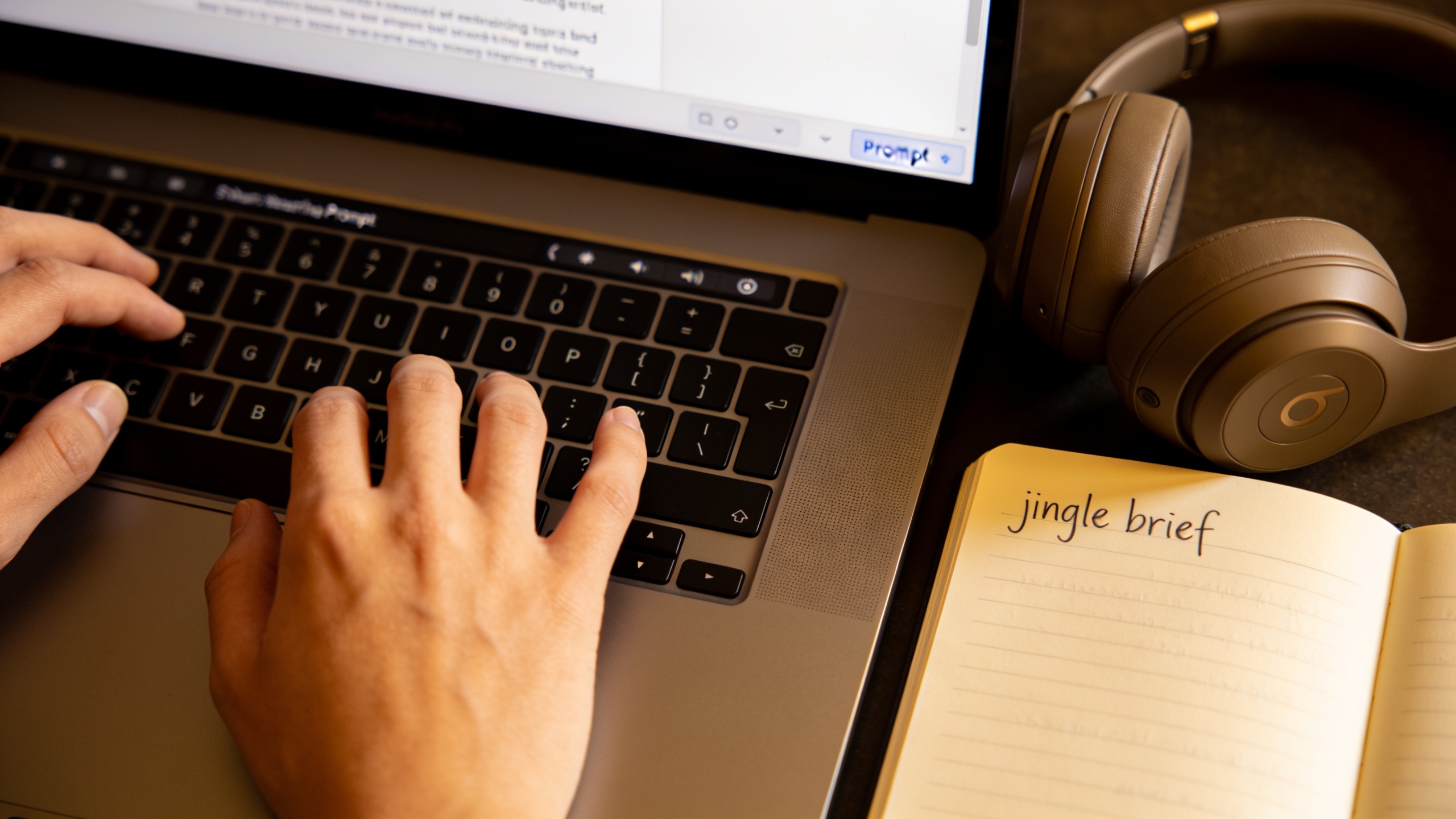 Typing a prompt for a jingle on laptop with headphones nearby